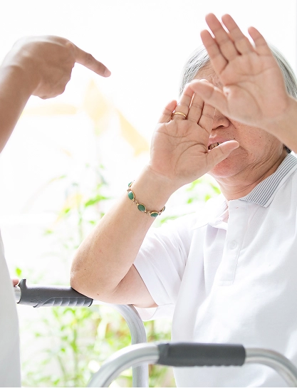 An elderly person in a wheelchair with a caregiver’s hand raised in front of them.